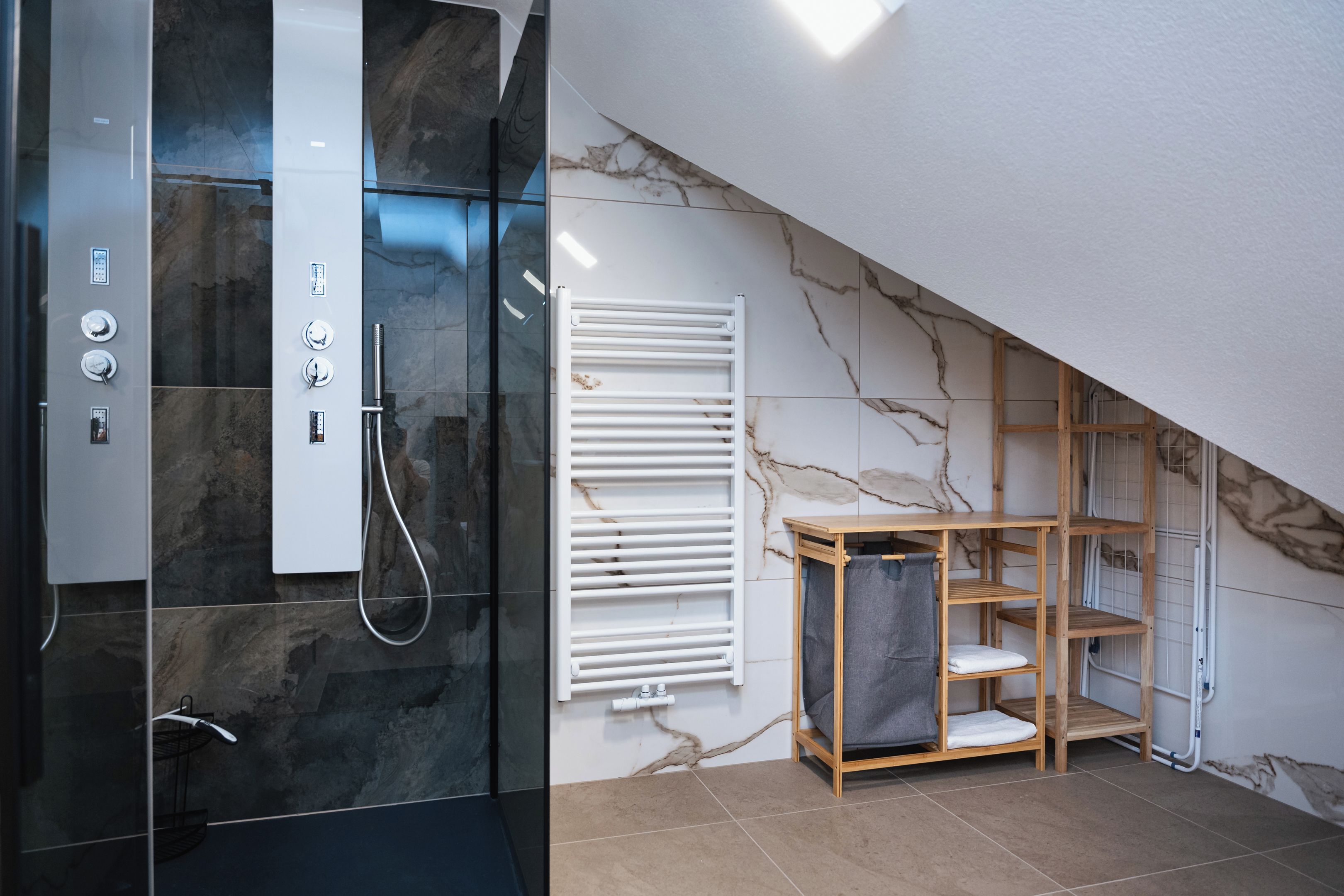 Un bagno moderno con doccia vetrata, un portasciugamani bianco e un mobiletto a mensole in legno.