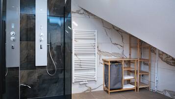 Un bagno moderno con doccia vetrata, un portasciugamani bianco e un mobiletto a mensole in legno.