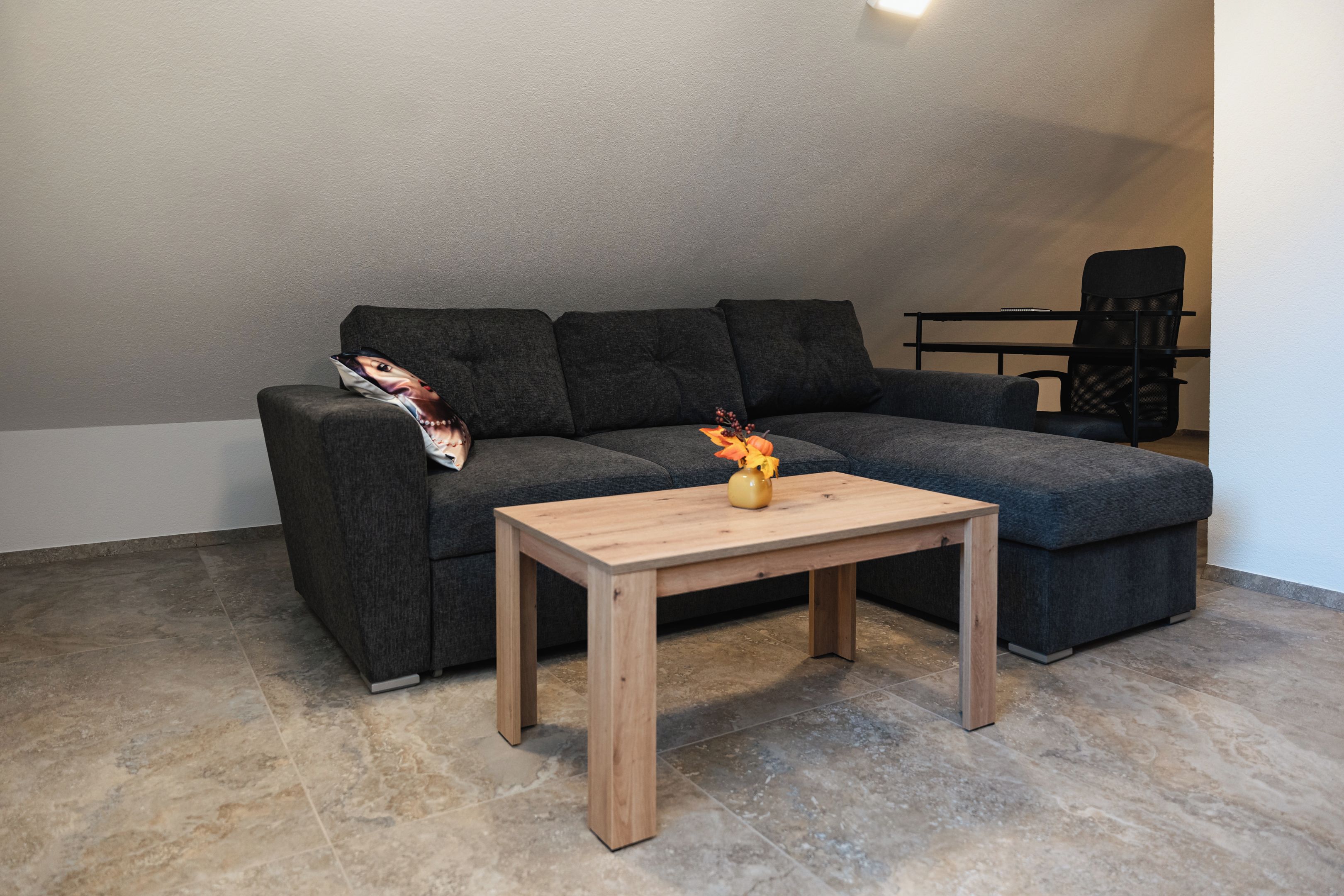 A modern living room with a sectional sofa, a small wooden coffee table, and a vase with flowers.