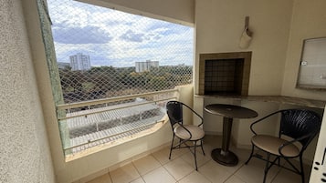 Varanda com vista para prédios e árvores, uma mesa pequena com cadeiras e piso de azulejos.