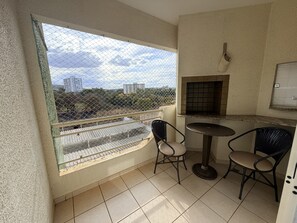 A balcony with a view of buildings and trees, a small table with chairs, and a tiled floor. - CRCN - Vitoria das Thermas (Caldas Novas)