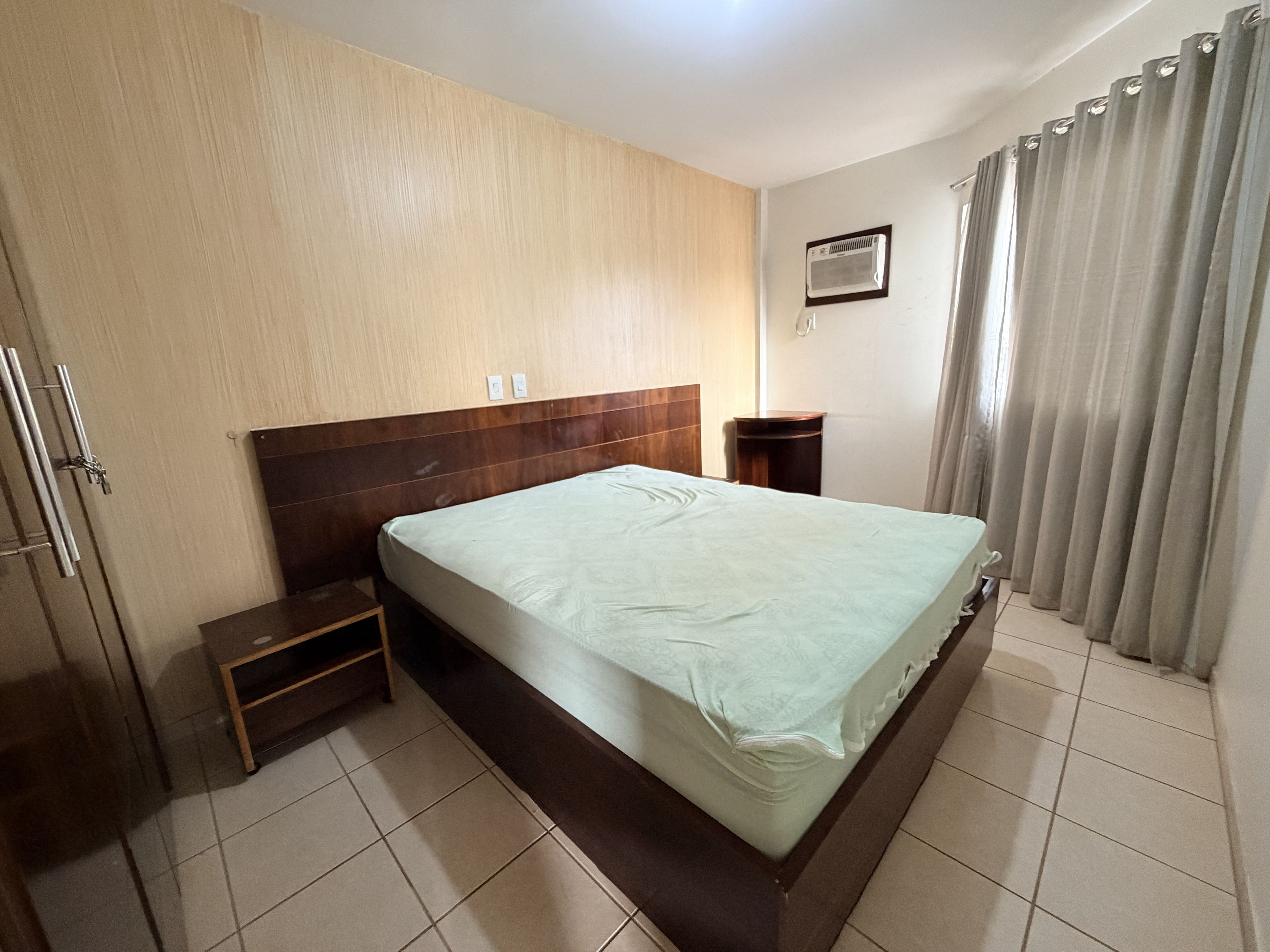 Une chambre d’hôtel avec un lit, une table de chevet, un climatiseur fixé au mur et une fenêtre avec des rideaux.