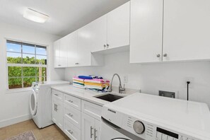 A laundry room with a washing machine, a stacked washer and dryer, a sink, and white cabinets. - Point of View - Sanibel Island House with Private Pool, Lake Views & Beach Access! (Sanibel)