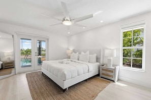 A bedroom with a bed, nightstands, a ceiling fan, and a view of the outdoors. - Point of View - Sanibel Island House with Private Pool, Lake Views & Beach Access! (Sanibel)