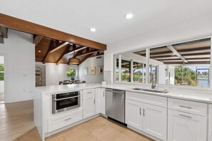 A modern kitchen with white cabinetry, stainless steel appliances, and a large window offering a view of the outdoors. - Point of View - Sanibel Island House with Private Pool, Lake Views & Beach Access! (Sanibel)