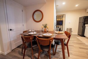 Un coin repas avec une table dressée pour quatre personnes, un miroir au mur et une cuisine en arrière-plan.