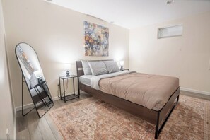 A bedroom with a bed, a standing mirror, a nightstand, and a painting on the wall. - 2 Bedroom / Full Kitchen (Grandview)