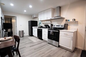 A modern kitchen with white cabinets, stainless steel appliances, and a dining area with a table and chairs. - 2 Bedroom / Full Kitchen (Grandview)