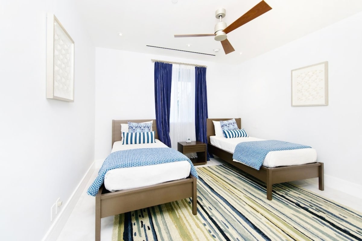 A hotel room with two beds, a ceiling fan, a window with curtains, and a patterned rug.