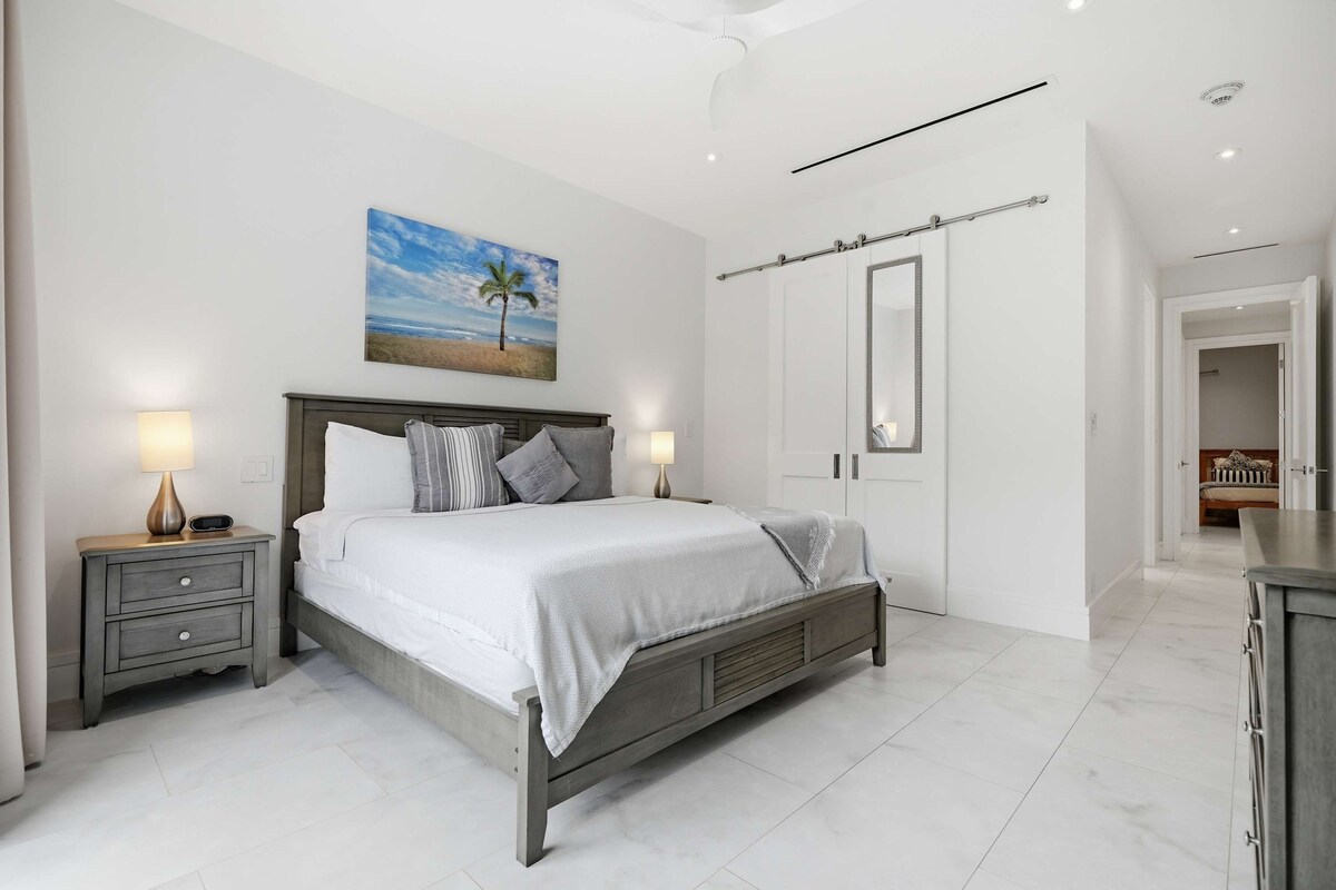 A bedroom with a bed, bedside tables, a nightstand, a mirror, and a door.