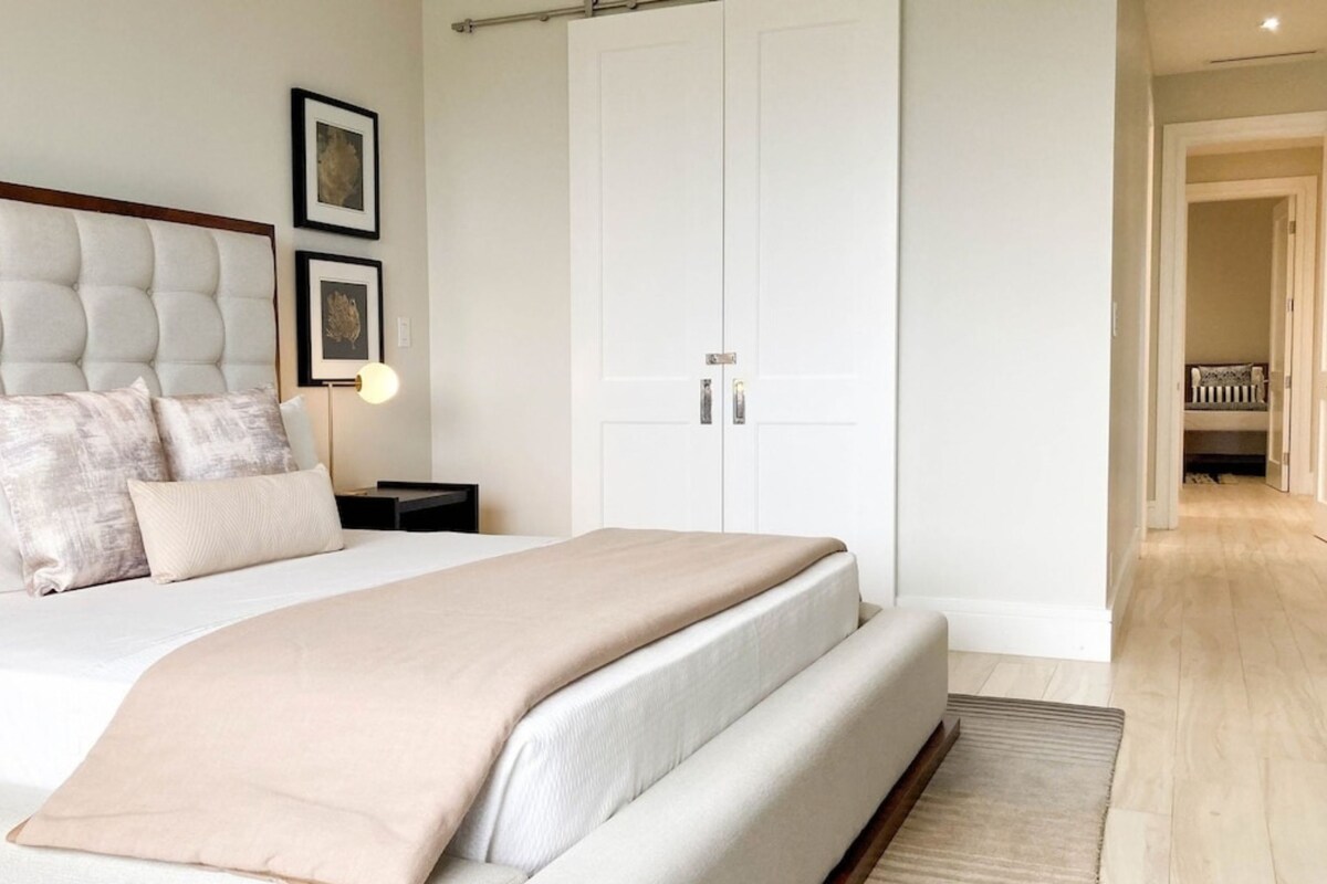 A bedroom with a large bed, a wardrobe, and a nightstand with a lamp.