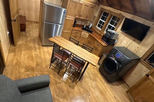 Cocina compacta con armarios de madera, refrigerador de acero inoxidable, lavadora y comedor con mesa y sillas.