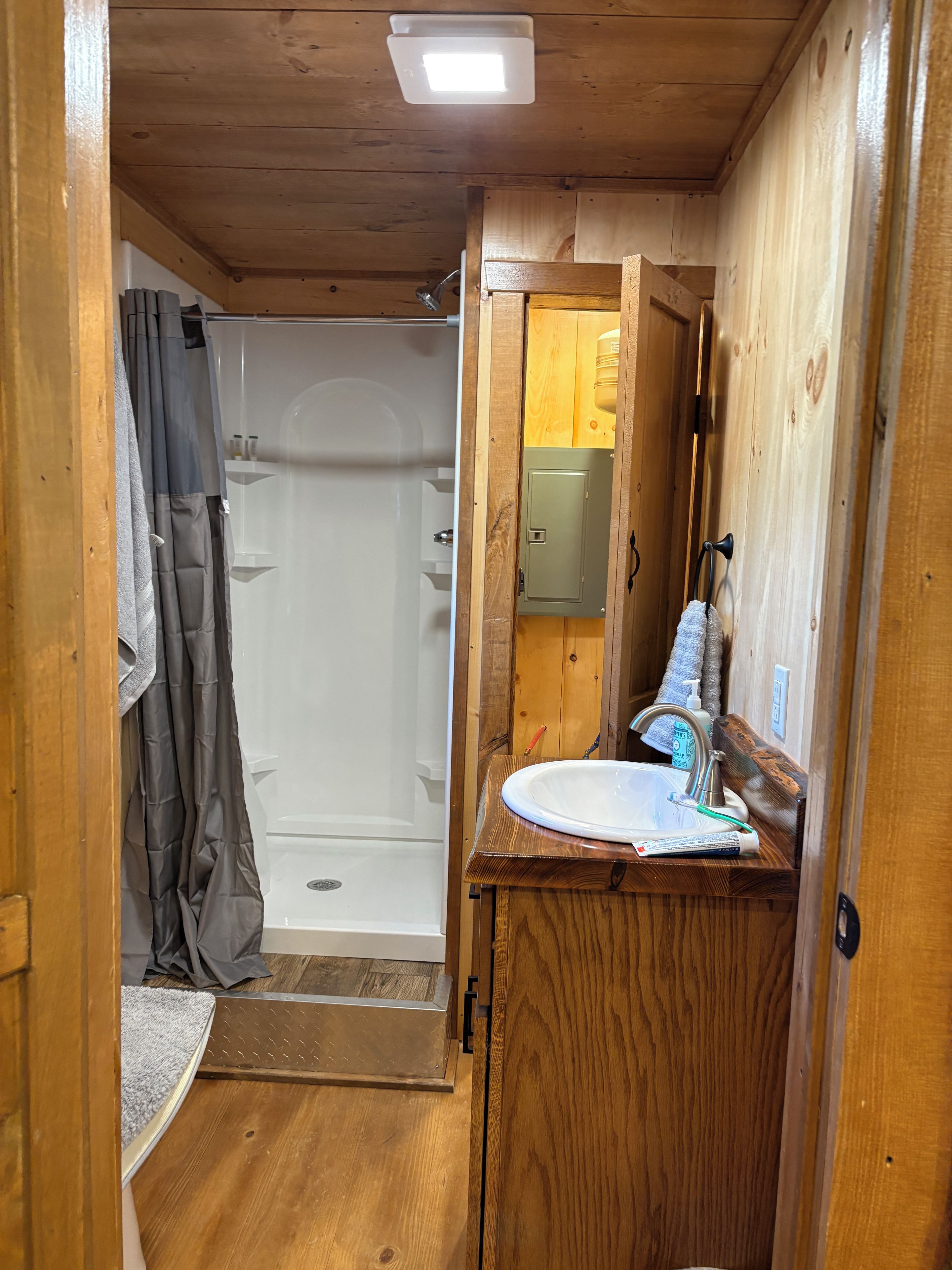 Une petite salle de bain en bois, équipée d’une douche, d’un lavabo et d’un miroir.