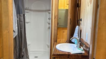 Une petite salle de bain en bois, équipée d’une douche, d’un lavabo et d’un miroir.