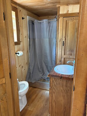 A wooden bathroom with a toilet, a shower curtain, and a sink.