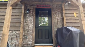 L’entrée d’un chalet en bois, avec un mur en pierre, une porte noire et un barbecue recouvert d’un tissu noir.