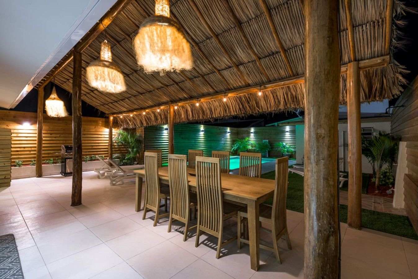 An outdoor dining area with a thatched roof, wooden chairs, and hanging light fixtures.