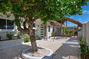 Un arbre à l’écorce épaisse et au feuillage dense, situé dans un espace aménagé avec un sol recouvert de gravier.