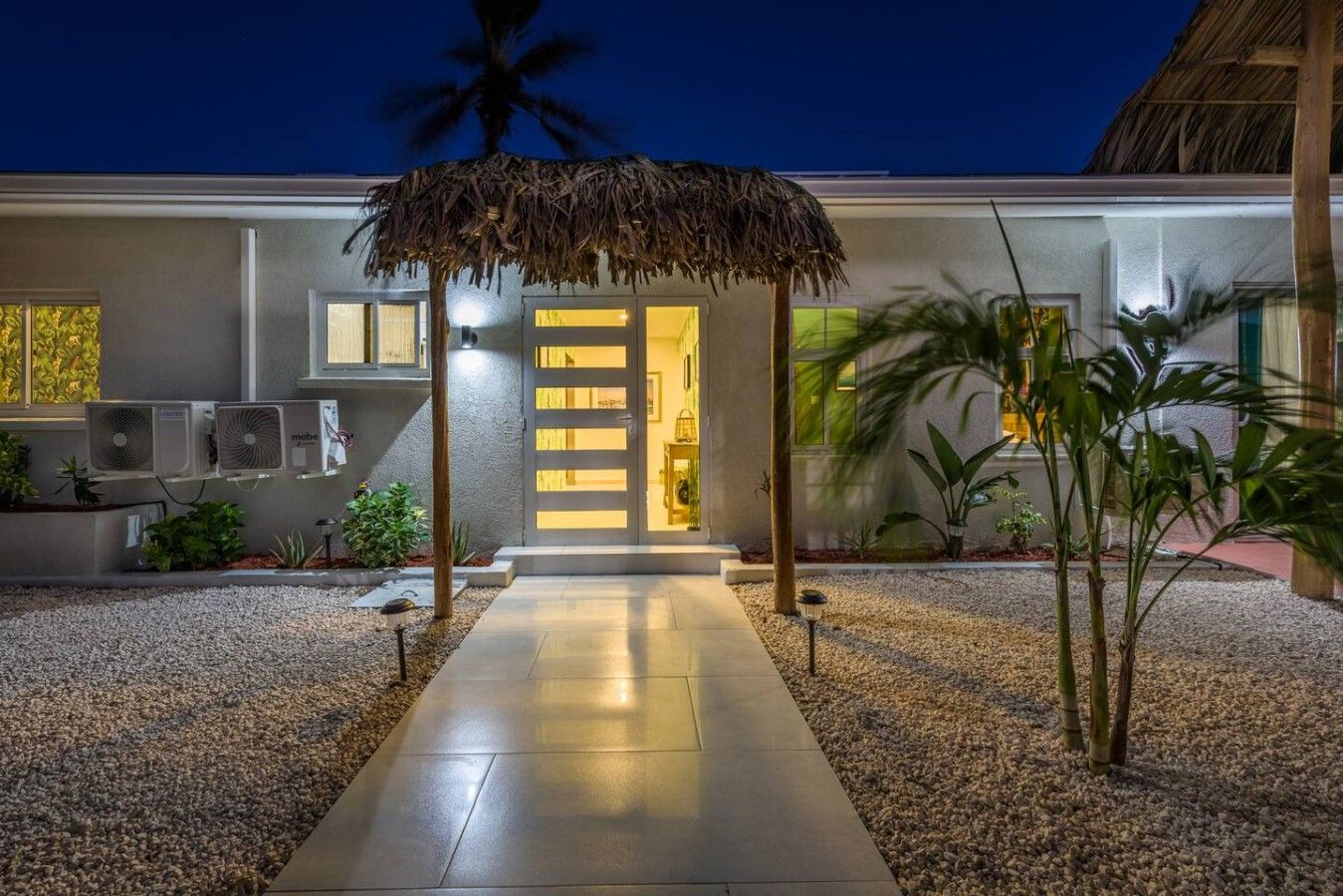 A modern building with a concrete pathway leading to a door with a thatched roof entrance.