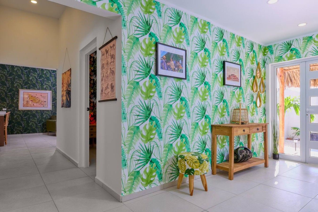 Une pièce dont le papier peint est orné de motifs de feuilles tropicales, avec une console en bois et des tableaux encadrés accrochés aux murs.