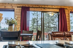Ein Holzblockbau-Innenraum mit Esstisch, Stühlen, einer Couch und einem großen Fenster mit Vorhängen.