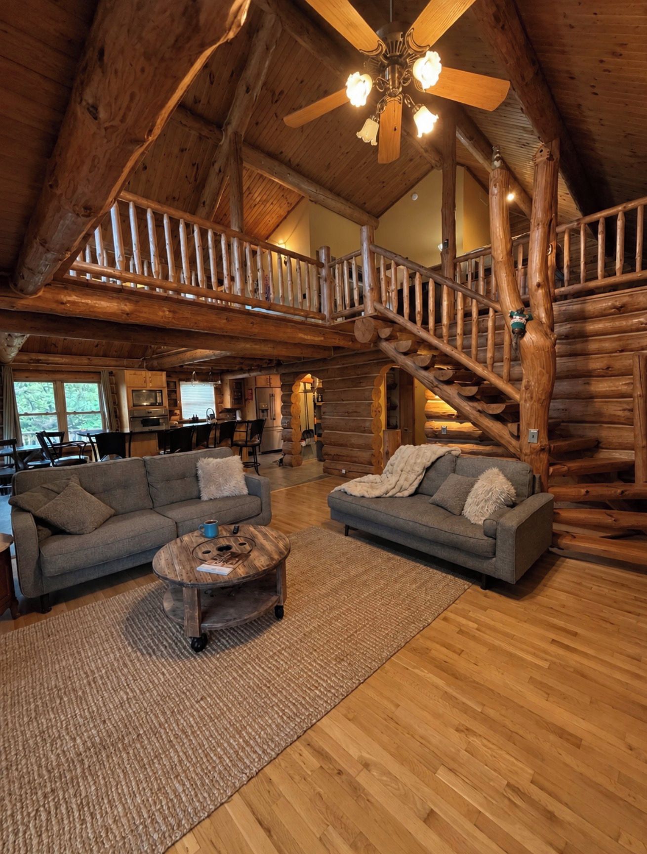Ein großzügiger Wohnbereich mit einer Holztreppe, zwei Sofas, einem Couchtisch und einem Deckenventilator.
