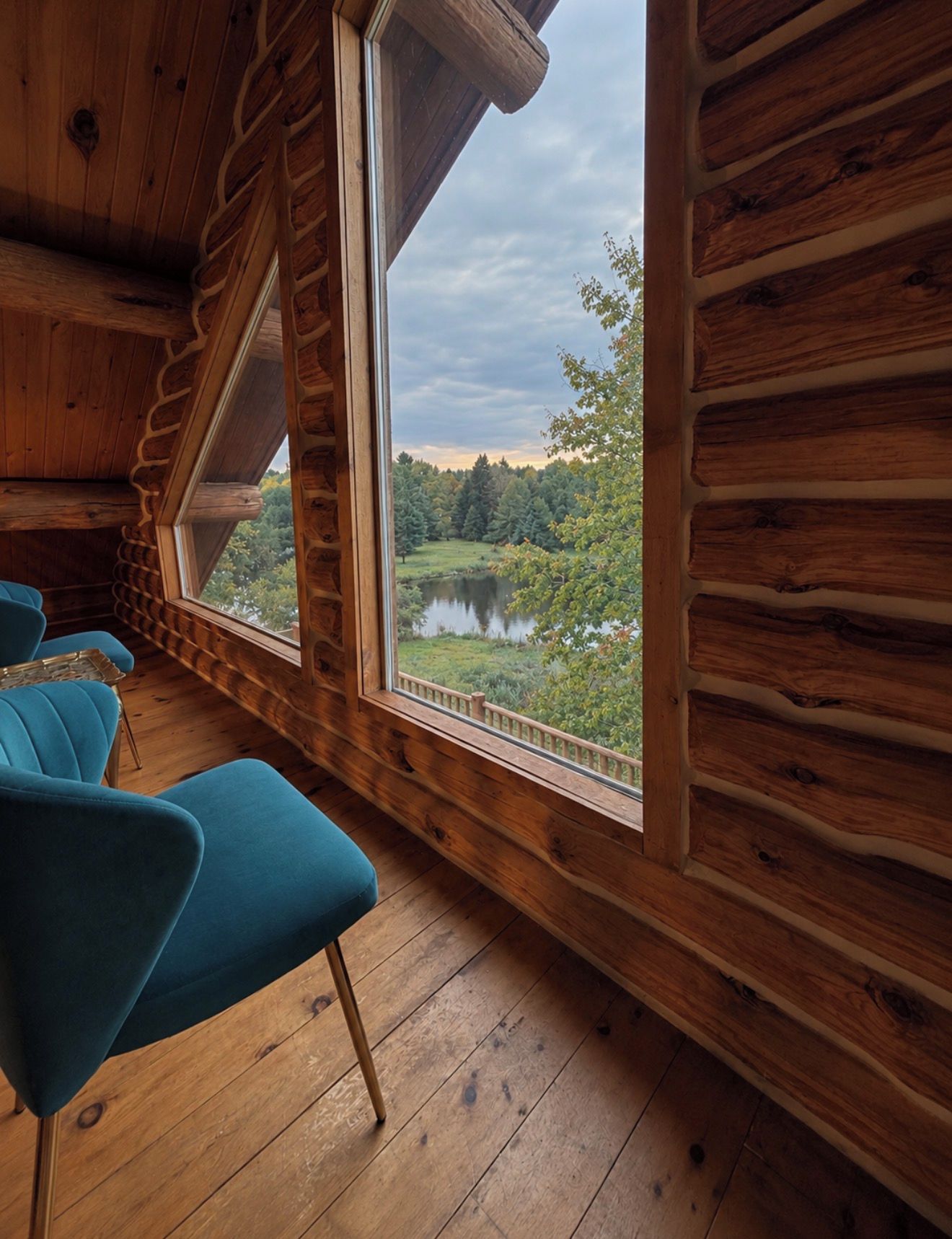 A cabin interior with a large window, wooden walls, and a blue chair.