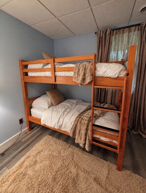 Ein Stockbett mit Holzgestell, weißer Bettwäsche und einer beigen Decke.