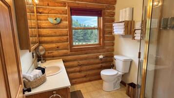Baño de cabaña de troncos con interior de madera, una ventana, un lavamanos, un inodoro y una zona de ducha.