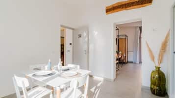 Uma área de refeições com mesa branca posta para quatro pessoas, parede de destaque em madeira e vista para outro cômodo.
