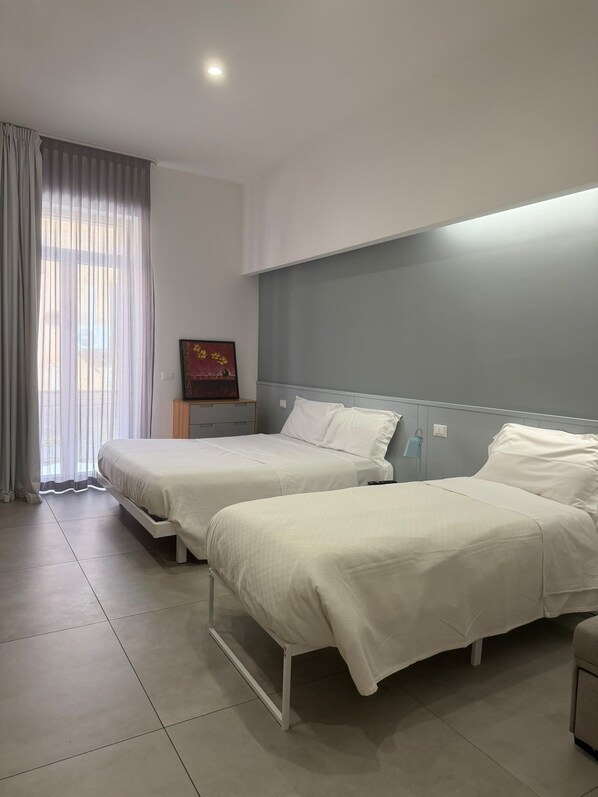 Habitación de hotel con dos camas, una mesita de noche, un cuadro y una ventana con cortinas.