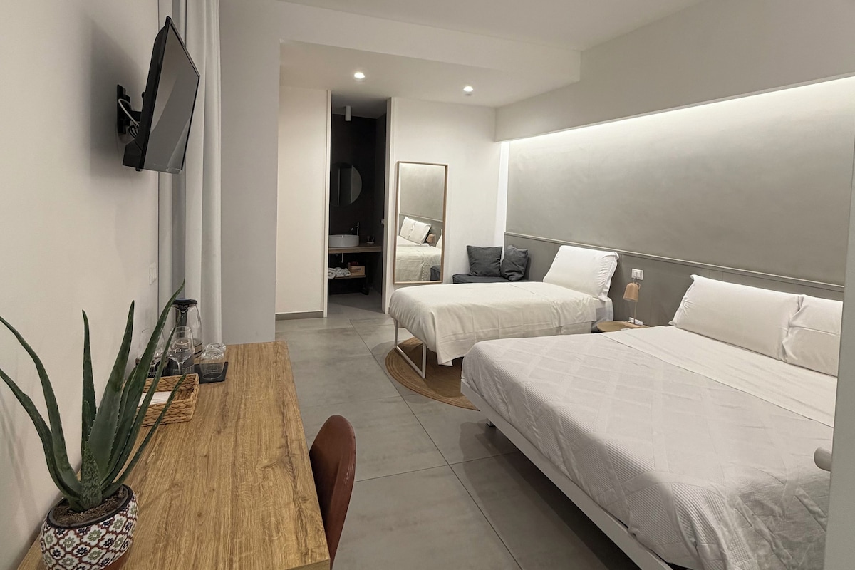 Una habitación de hotel moderna con un escritorio de madera, dos camas, un televisor de pantalla plana y un espejo.