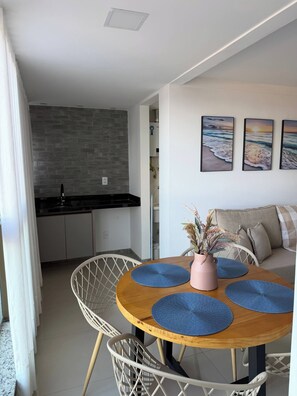 A dining area with a round table, blue placemats, a pink vase with dried flowers, and a white chair. - Incredible Ocean View 2 Bedrooms | Itaparica Beach (Vila Velha)