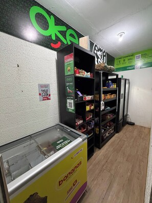 A refrigerated display case with a banana brand product, shelves stocked with various packaged goods, and a QR code for group participation. - Incredible Ocean View 2 Bedrooms | Itaparica Beach (Vila Velha)