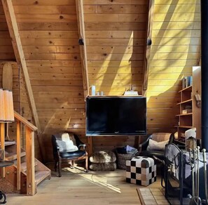 Een gezellig houten interieur met een televisie, zithoek en een trap.