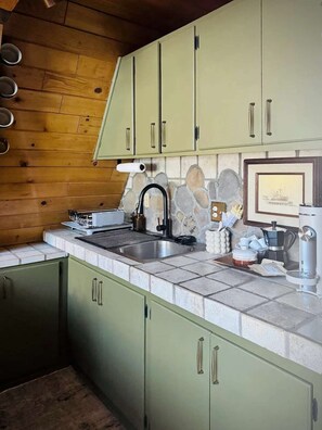 A kitchen with green cabinets, a stone backsplash, and a coffee maker. - The Highpoint A-Frame | Walkable | BBQ | Max 4 (Big Bear Lake)