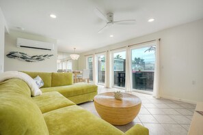 A modern living room with a green sofa, a round wicker coffee table, and a ceiling fan. - Mermaid Cove With Beach Days & Hot Tub Nights! AC, Ocean, Pool/HotTub (Oceanside)