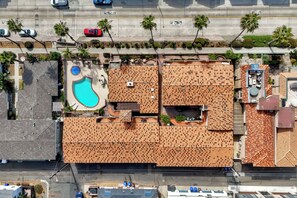 An aerial view of a residential area with a swimming pool, multiple buildings with tiled roofs, and a road with vehicles. - Mermaid Cove With Beach Days & Hot Tub Nights! AC, Ocean, Pool/HotTub (Oceanside)