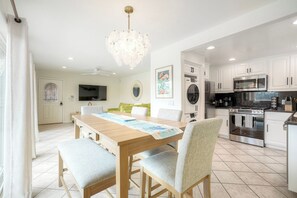 A modern kitchen with white cabinets, stainless steel appliances, and a dining area with a wooden table and chairs. - Mermaid Cove With Beach Days & Hot Tub Nights! AC, Ocean, Pool/HotTub (Oceanside)