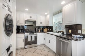 A modern kitchen with white cabinetry, stainless steel appliances, and a granite countertop. - Mermaid Cove With Beach Days & Hot Tub Nights! AC, Ocean, Pool/HotTub (Oceanside)