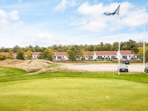 A golf course with a flagpole, a building with a red roof, and a flag. - 4 Star Holiday Home in Laeso (Læsø)