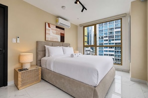 Ein modernes Hotelzimmer mit einem großen Bett, einer Nachttischlampe, einer Klimaanlage und Blick auf die Stadt durch ein großes Fenster.