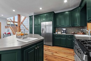 A modern kitchen with green cabinets, stainless steel appliances, and a wooden floor. - Helen Haus: Golf Sim & Hot Tub Theater Retreat (Helen)