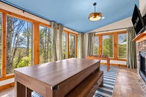 Una habitación con una mesa de madera, una mesa de futbolín y una chimenea.