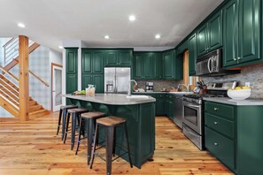 Una cocina con gabinetes verdes, un refrigerador de acero inoxidable, un horno empotrado y una zona de bar con taburetes.