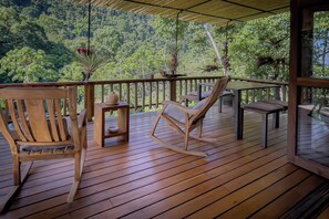 Eine Holzterrasse mit zwei Schaukelstühlen und einem Tisch, mit Blick auf einen üppigen grünen Wald.