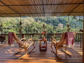 A wooden deck with two rocking chairs and a table, overlooking a lush forest.