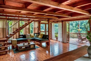 A wooden interior with a staircase, a sofa, a coffee table, and a view of the outdoors. - Kubla Khan - Chirripó Riverfront Chalet (Perez Zeledon)