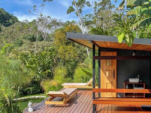 A wooden deck with two lounge chairs, a small pond, and a building with a door and a sink. - Kubla Khan - Chirripó Riverfront Chalet (Perez Zeledon)