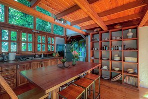 A wooden kitchen with a central island, wooden cabinets, and a view of greenery outside.